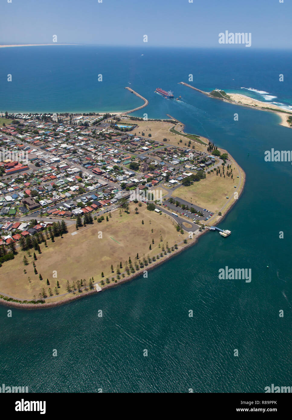 Eine Kohle Schiff verlässt Newcastle Hafen für eine ausländische Ziel gebunden. Der hafenseite surburb von Stockton und Nobbys Beach auf beiden Seiten der ha Stockfoto
