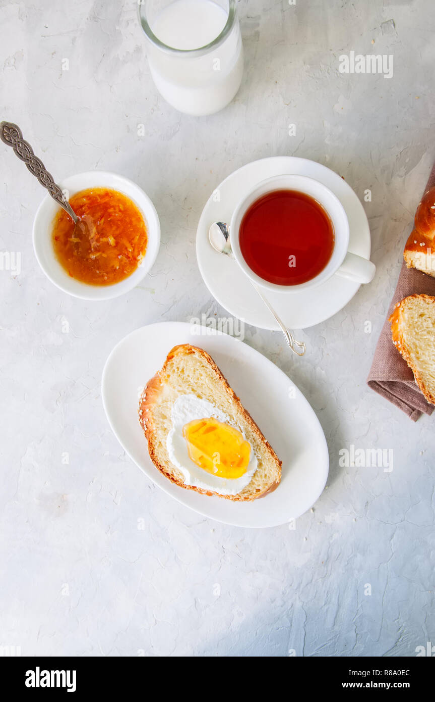 Scheibe hausgemachten Sesamsamen challah Brot mit Marmelade, ein Glas Milch und eine Tasse Tee auf einem weißen Hintergrund. Frühstück Konzept. Stockfoto