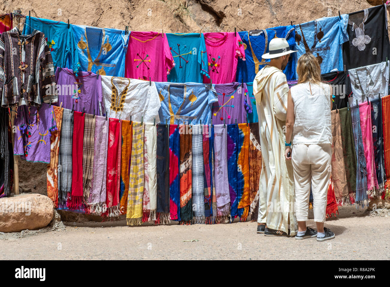 Ein paar Touristen halt an bunte traditionelle Kleidung zum Verkauf an Todra-schlucht, Tinghir, Marokko zu suchen Stockfoto