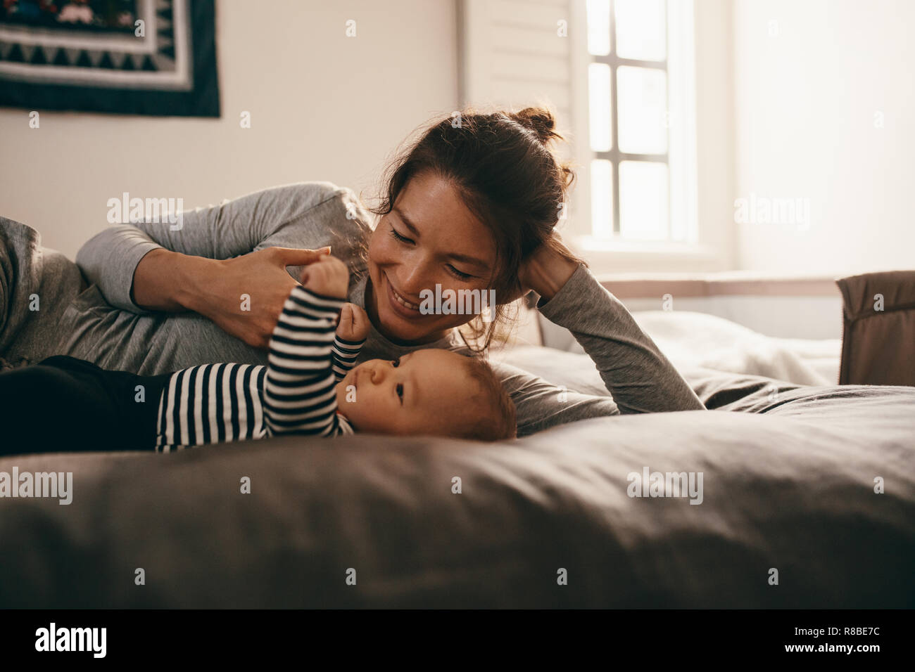 Frau liegend auf Bett verwöhnen ihr Baby. Lächelnde Mutter spielt mit ihrem Kind Baby liegend auf Bett zu Hause. Stockfoto