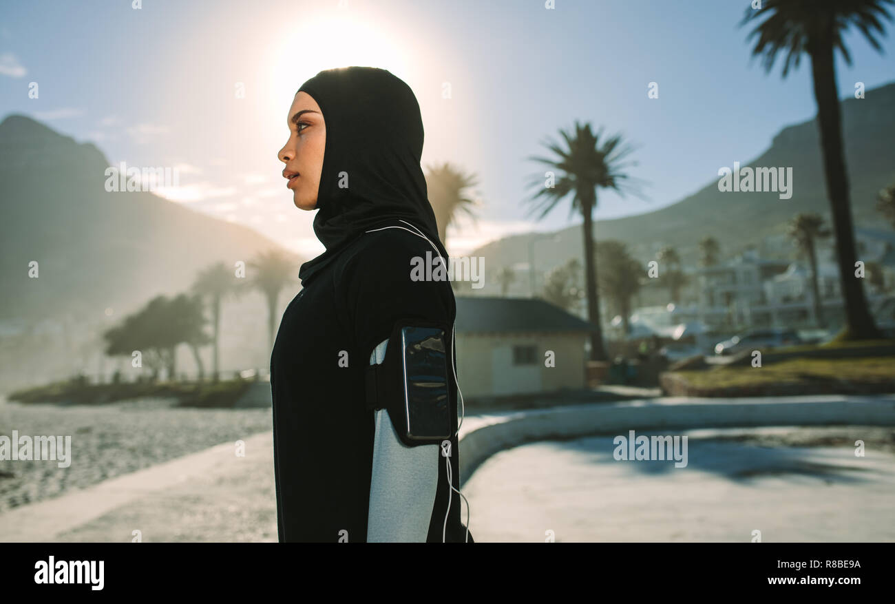 Seitenansicht des Jungen hijab Frau, die draußen mit hellem Sonnenlicht zurück. Muslimische Frau Ausruhen nach einem morgendlichen Lauf in der Stadt. Stockfoto