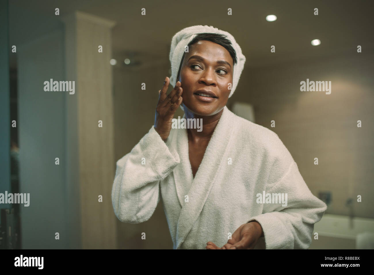 Reflexion der Afrikanischen Frau im Badezimmer spiegel Anwendung kosmetische Creme im Gesicht. Reife weibliche setzen auf Feuchtigkeitscreme auf ihr Gesicht haut. Stockfoto