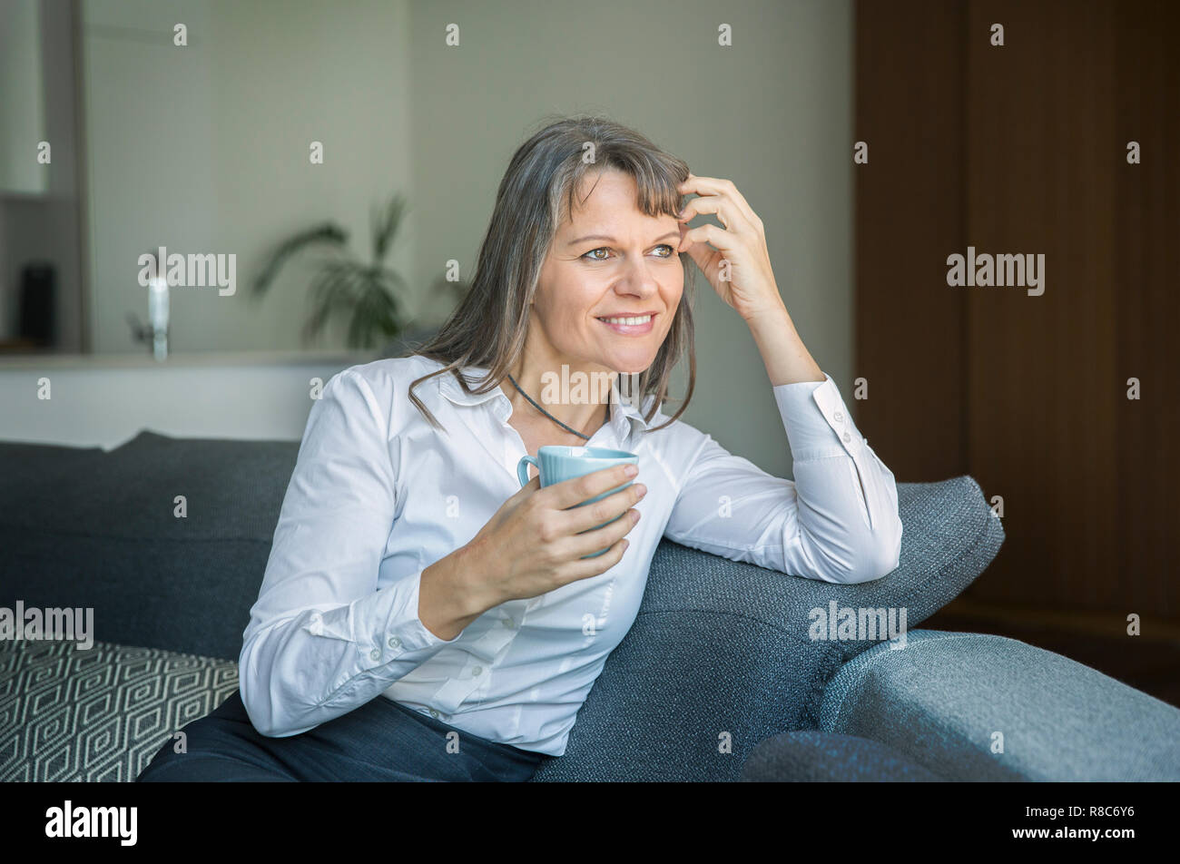 Frau mittleren Alters, die in förmlichen ware Holding eine Tasse Kaffee in ihre Stadt apartment Stockfoto