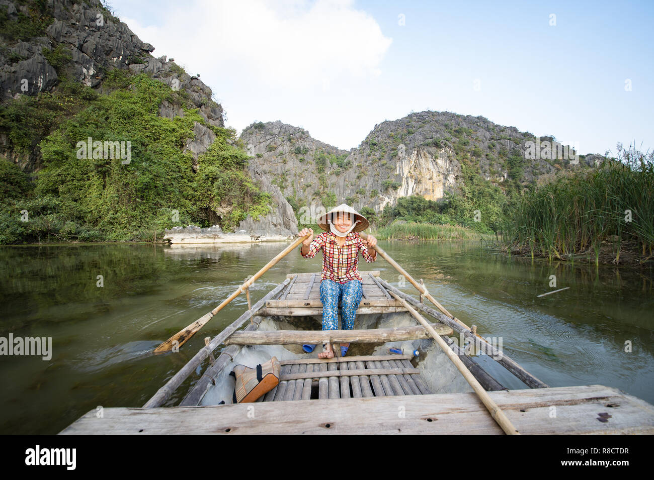 Ein lächelndes vietnamesische Frau mit ihrem traditionellen hat ist ein hölzernes Boot in der Ninh Binh Kanal. Vietnam. Stockfoto