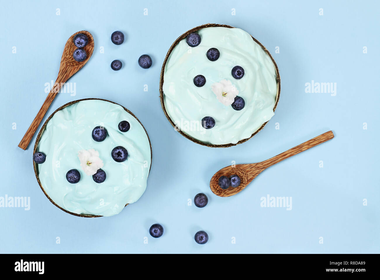 Blue spirulina und Berry Smoothie Schüssel, frisches Obst mit Holzlöffel in Coconut serviert Schalen über einen blauen Hintergrund mit weißen Blumen. Bild shot f Stockfoto