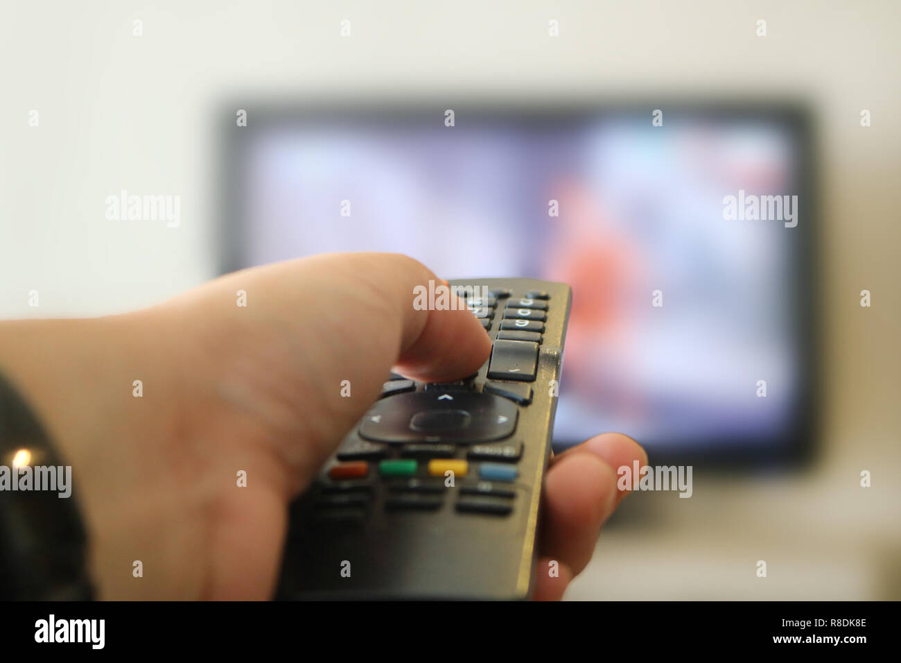 Bild einer Hand Klicken TV-Fernbedienung mit out of focus Fernsehen im Hintergrund Stockfoto