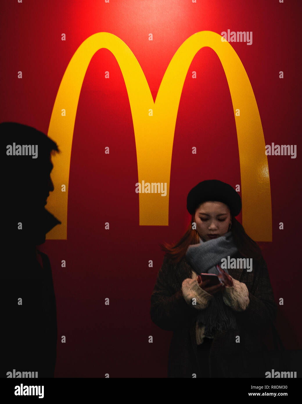 Ein Mädchen auf Ihrem Telefon durch eine Wand mit Mc Donald Logo auf. Sapporo, Hokkaido, Japan. Stockfoto