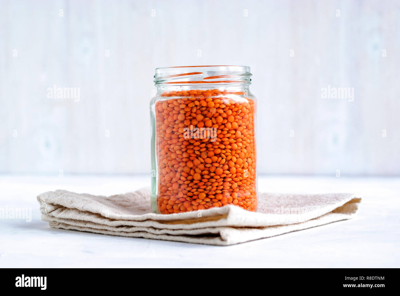 Glas Glas gefüllt mit orange oder rote Linsen angezeigte Seite auf das Stehen auf einem gefalteten Küche Tuch über einen weißen Hintergrund Stockfoto