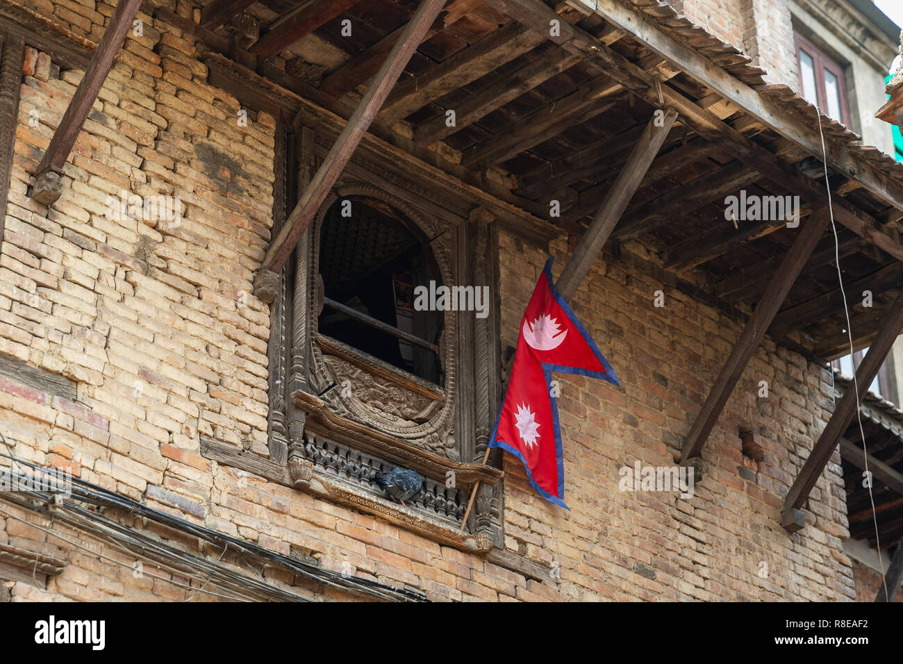 Nepalesische Flagge aufhängen außerhalb einer Holz Fenster in Patan, Kathmandu, Nepal geschnitzt. Stockfoto