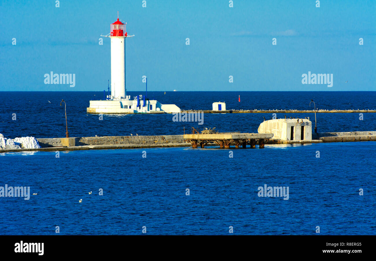 Ein Leuchtturm im Meer am Eingang zum Hafen vor dem Hintergrund eines schönen Abends blauer Himmel in weichen Farben. Sommer Seascape. Weiße Leucht Stockfoto