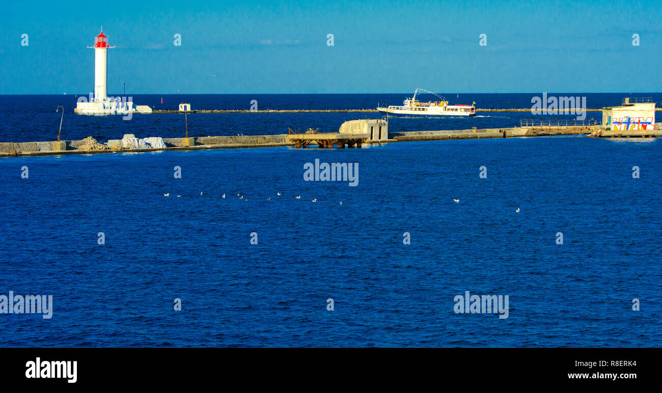 Ein Leuchtturm im Meer am Eingang zum Hafen vor dem Hintergrund eines schönen Abends blauer Himmel in weichen Farben. Sommer Seascape. Weiße Leucht Stockfoto