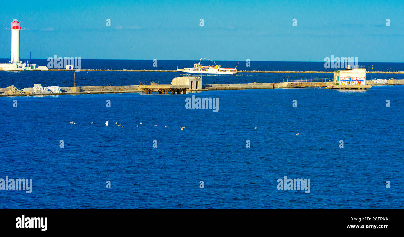 Ein Leuchtturm im Meer am Eingang zum Hafen vor dem Hintergrund eines schönen Abends blauer Himmel in weichen Farben. Sommer Seascape. Weiße Leucht Stockfoto