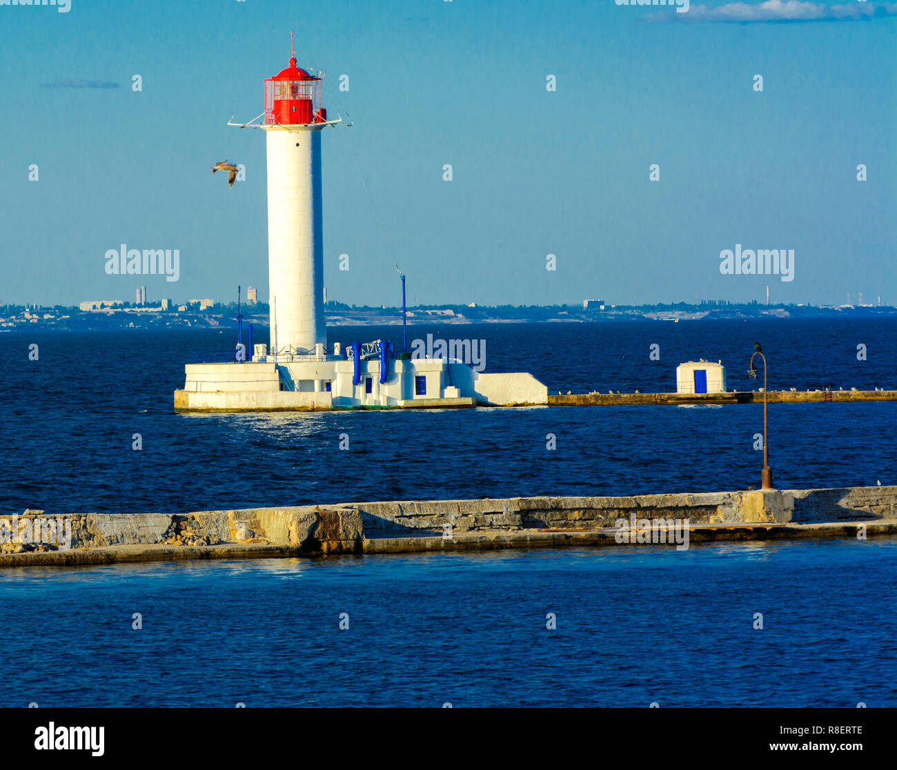 Ein Leuchtturm im Meer am Eingang zum Hafen vor dem Hintergrund eines schönen Abends blauer Himmel in weichen Farben. Sommer Seascape. Weiße Leucht Stockfoto