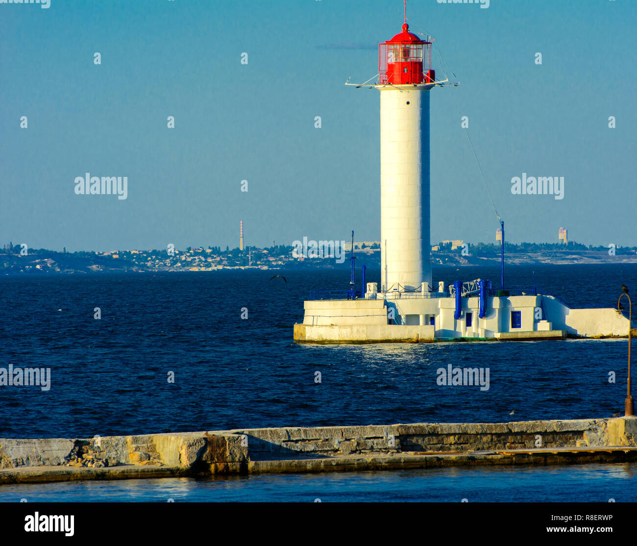 Ein Leuchtturm im Meer am Eingang zum Hafen vor dem Hintergrund eines schönen Abends blauer Himmel in weichen Farben. Sommer Seascape. Weiße Leucht Stockfoto