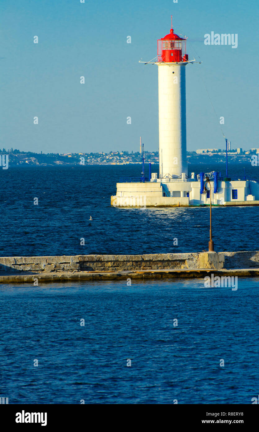 Ein Leuchtturm im Meer am Eingang zum Hafen vor dem Hintergrund eines schönen Abends blauer Himmel in weichen Farben. Sommer Seascape. Weiße Leucht Stockfoto