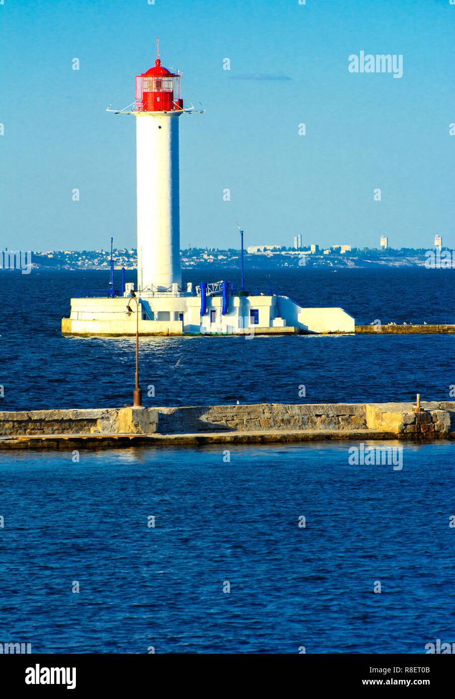 Ein Leuchtturm im Meer am Eingang zum Hafen vor dem Hintergrund eines schönen Abends blauer Himmel in weichen Farben. Sommer Seascape. Weiße Leucht Stockfoto