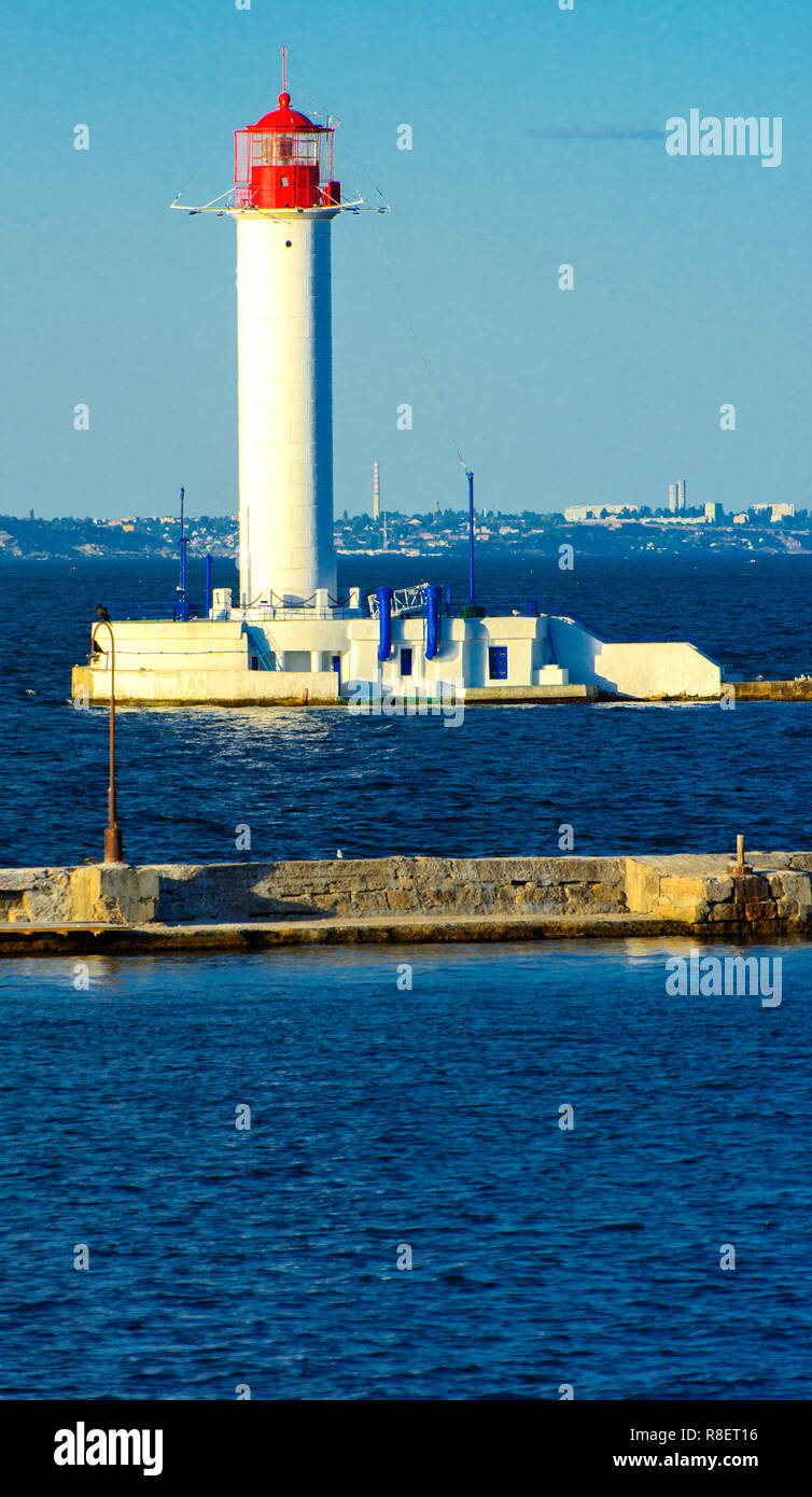 Ein Leuchtturm im Meer am Eingang zum Hafen vor dem Hintergrund eines schönen Abends blauer Himmel in weichen Farben. Sommer Seascape. Weiße Leucht Stockfoto