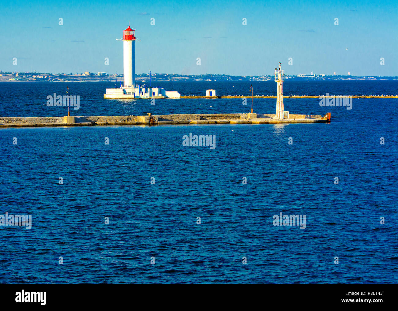Ein Leuchtturm im Meer am Eingang zum Hafen vor dem Hintergrund eines schönen Abends blauer Himmel in weichen Farben. Sommer Seascape. Weiße Leucht Stockfoto