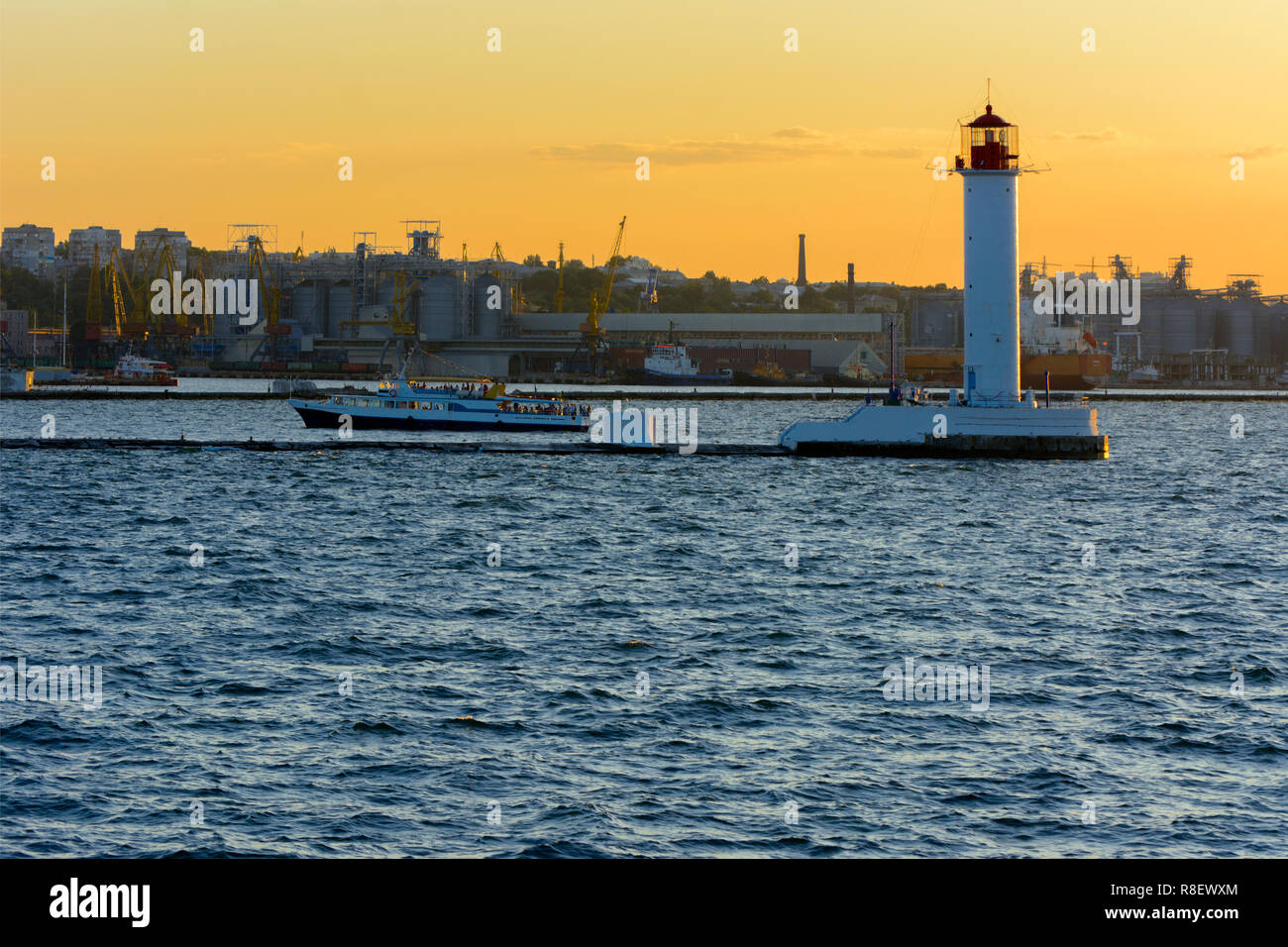Ein Leuchtturm im Meer am Eingang zum Hafen vor dem Hintergrund eines schönen Abends blauer Himmel in weichen Farben. Sommer Seascape. Weiße Leucht Stockfoto