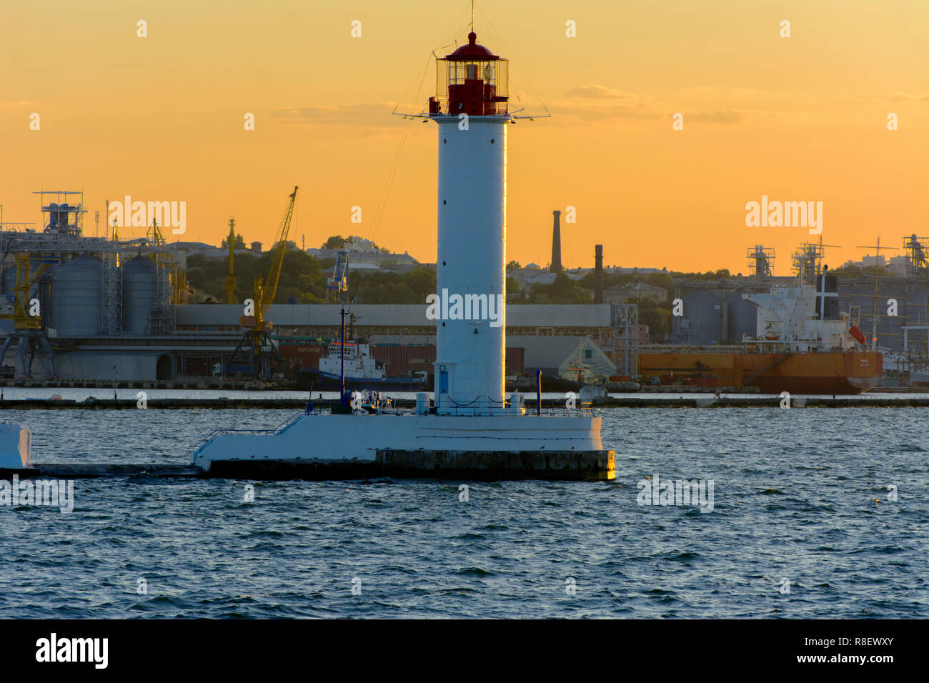 Ein Leuchtturm im Meer am Eingang zum Hafen vor dem Hintergrund eines schönen Abends blauer Himmel in weichen Farben. Sommer Seascape. Weiße Leucht Stockfoto