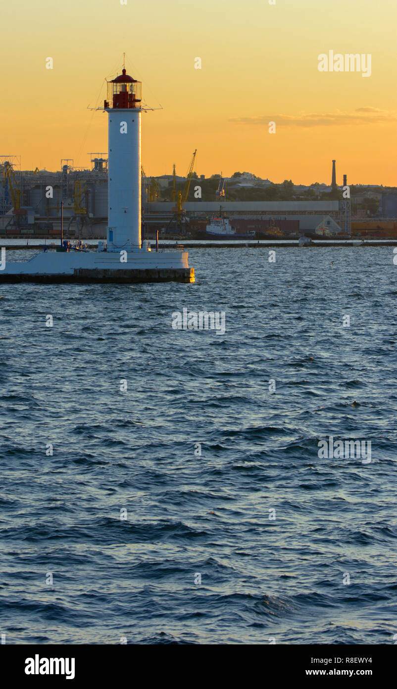 Ein Leuchtturm im Meer am Eingang zum Hafen vor dem Hintergrund eines schönen Abends blauer Himmel in weichen Farben. Sommer Seascape. Weiße Leucht Stockfoto