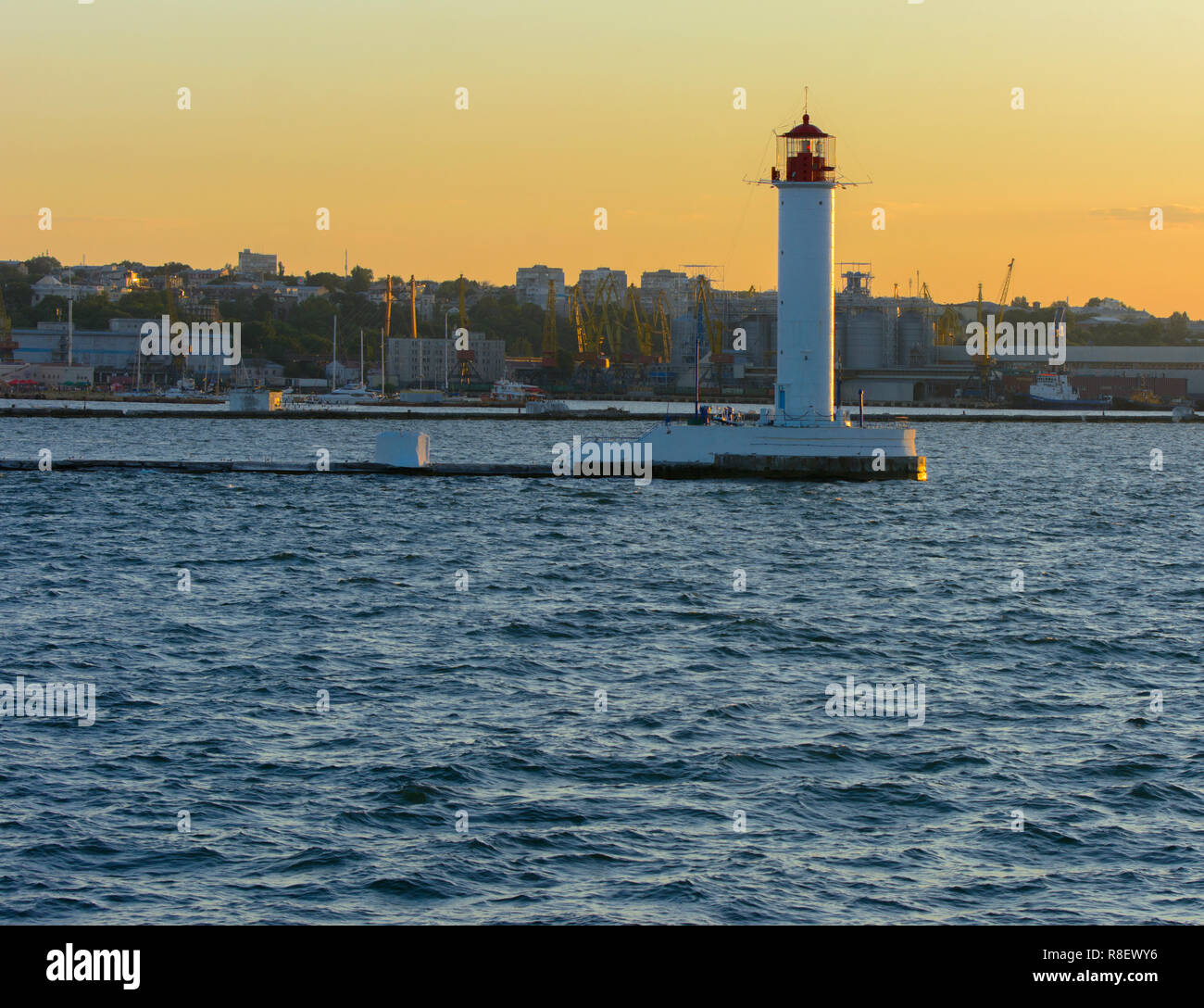 Ein Leuchtturm im Meer am Eingang zum Hafen vor dem Hintergrund eines schönen Abends blauer Himmel in weichen Farben. Sommer Seascape. Weiße Leucht Stockfoto