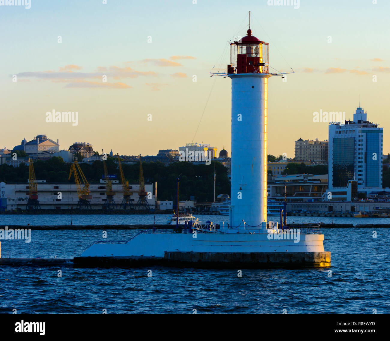 Ein Leuchtturm im Meer am Eingang zum Hafen vor dem Hintergrund eines schönen Abends blauer Himmel in weichen Farben. Sommer Seascape. Weiße Leucht Stockfoto