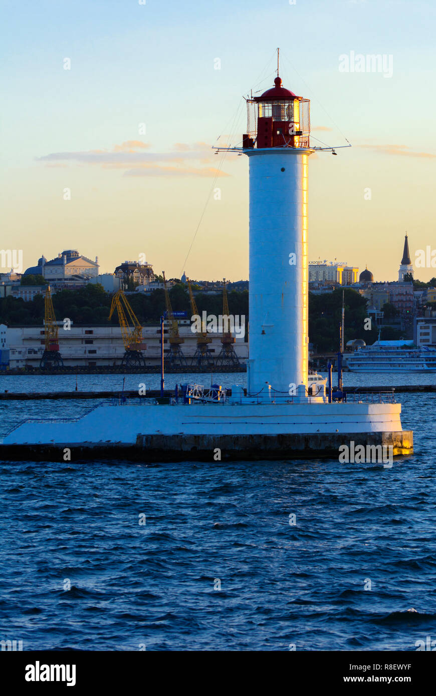 Ein Leuchtturm im Meer am Eingang zum Hafen vor dem Hintergrund eines schönen Abends blauer Himmel in weichen Farben. Sommer Seascape. Weiße Leucht Stockfoto