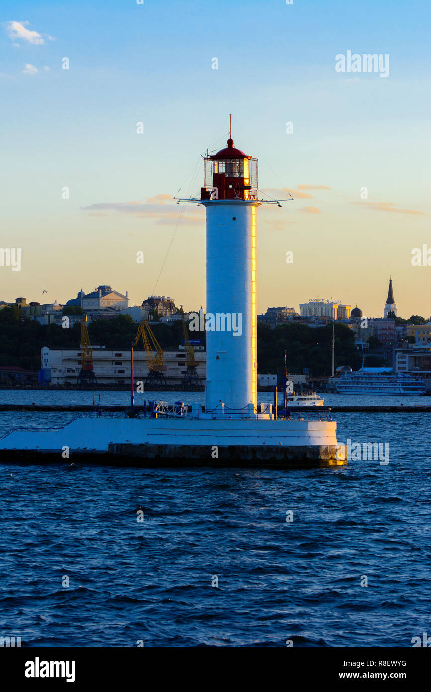 Ein Leuchtturm im Meer am Eingang zum Hafen vor dem Hintergrund eines schönen Abends blauer Himmel in weichen Farben. Sommer Seascape. Weiße Leucht Stockfoto
