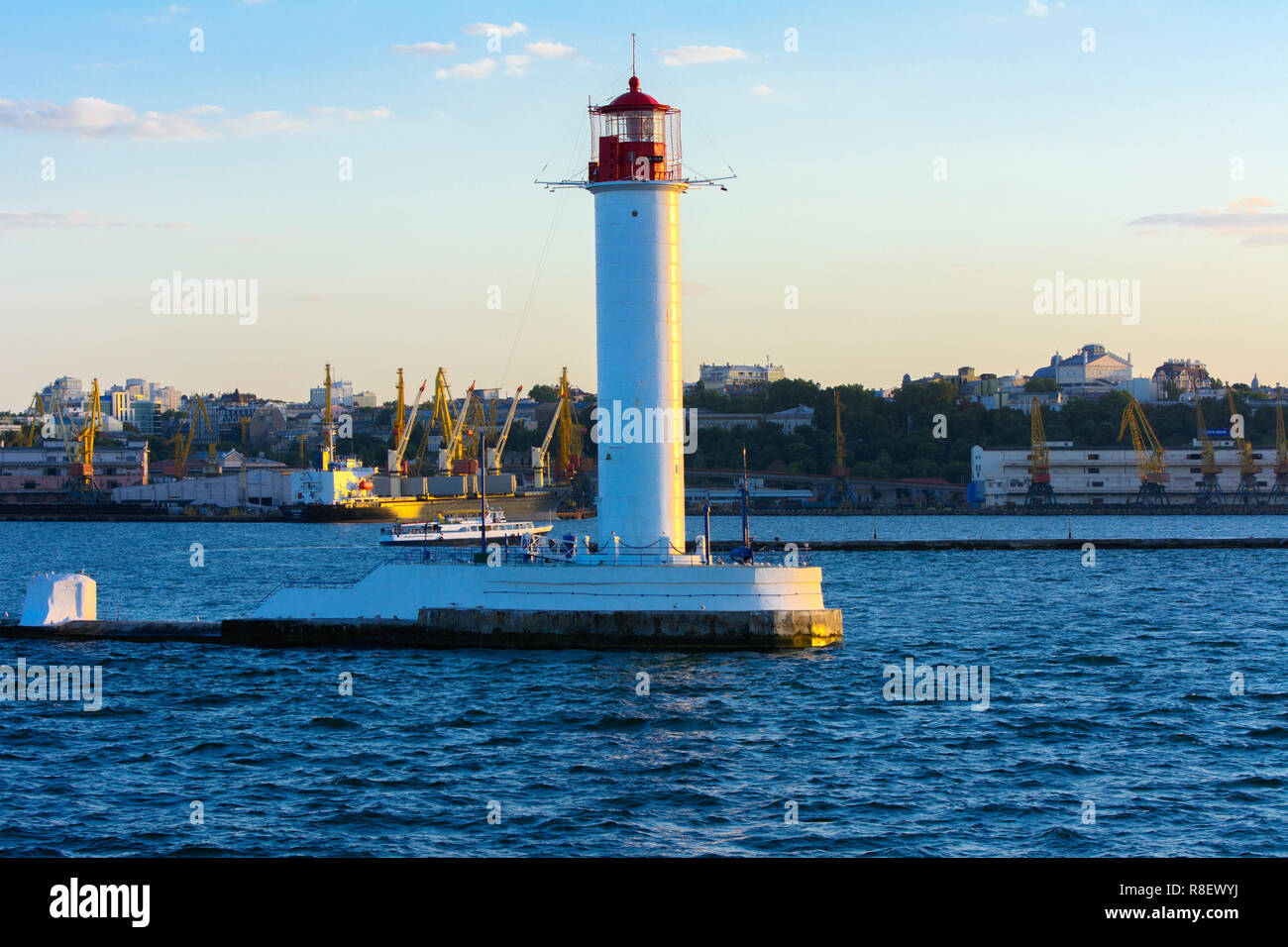 Ein Leuchtturm im Meer am Eingang zum Hafen vor dem Hintergrund eines schönen Abends blauer Himmel in weichen Farben. Sommer Seascape. Weiße Leucht Stockfoto