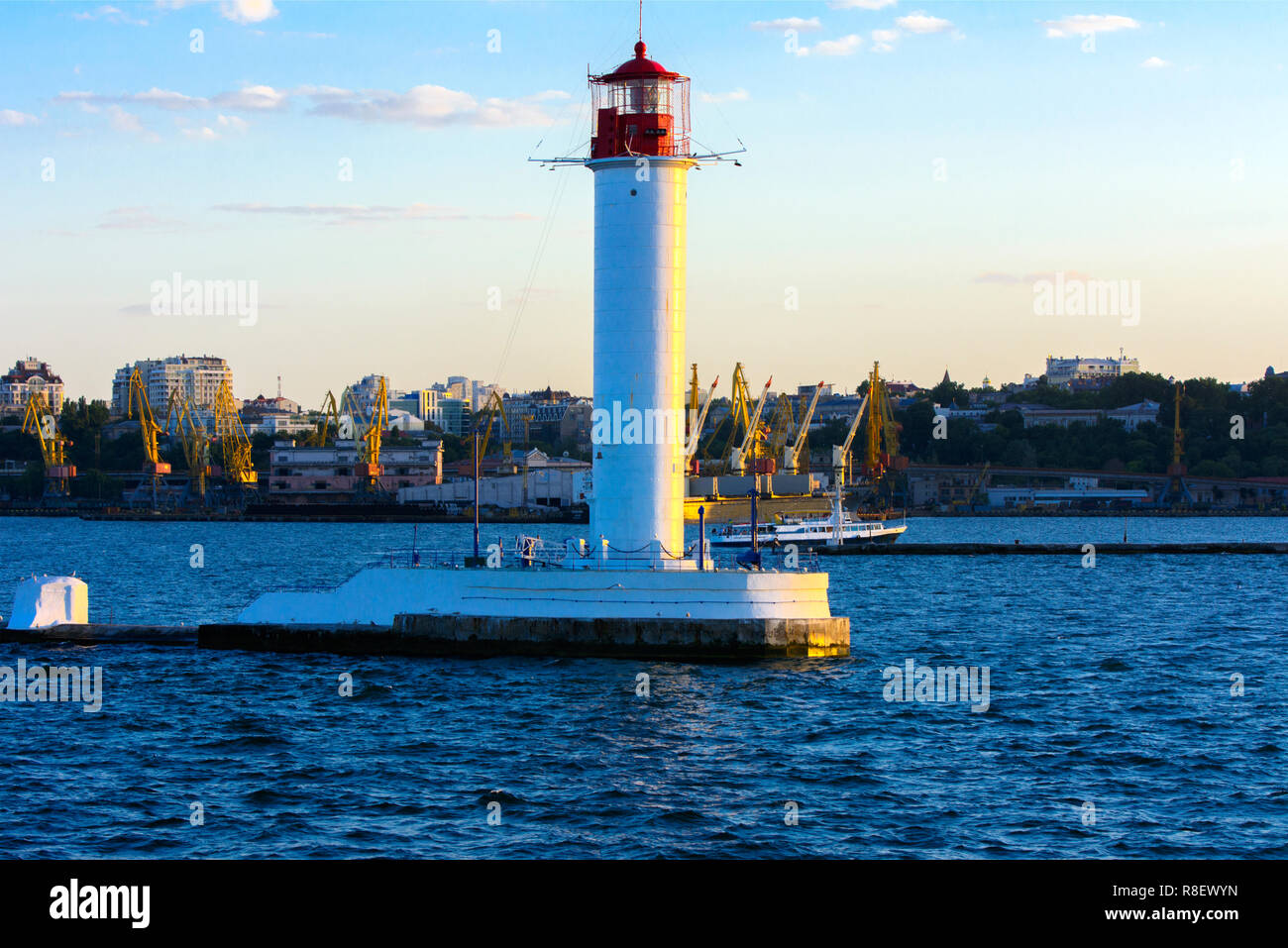Ein Leuchtturm im Meer am Eingang zum Hafen vor dem Hintergrund eines schönen Abends blauer Himmel in weichen Farben. Sommer Seascape. Weiße Leucht Stockfoto