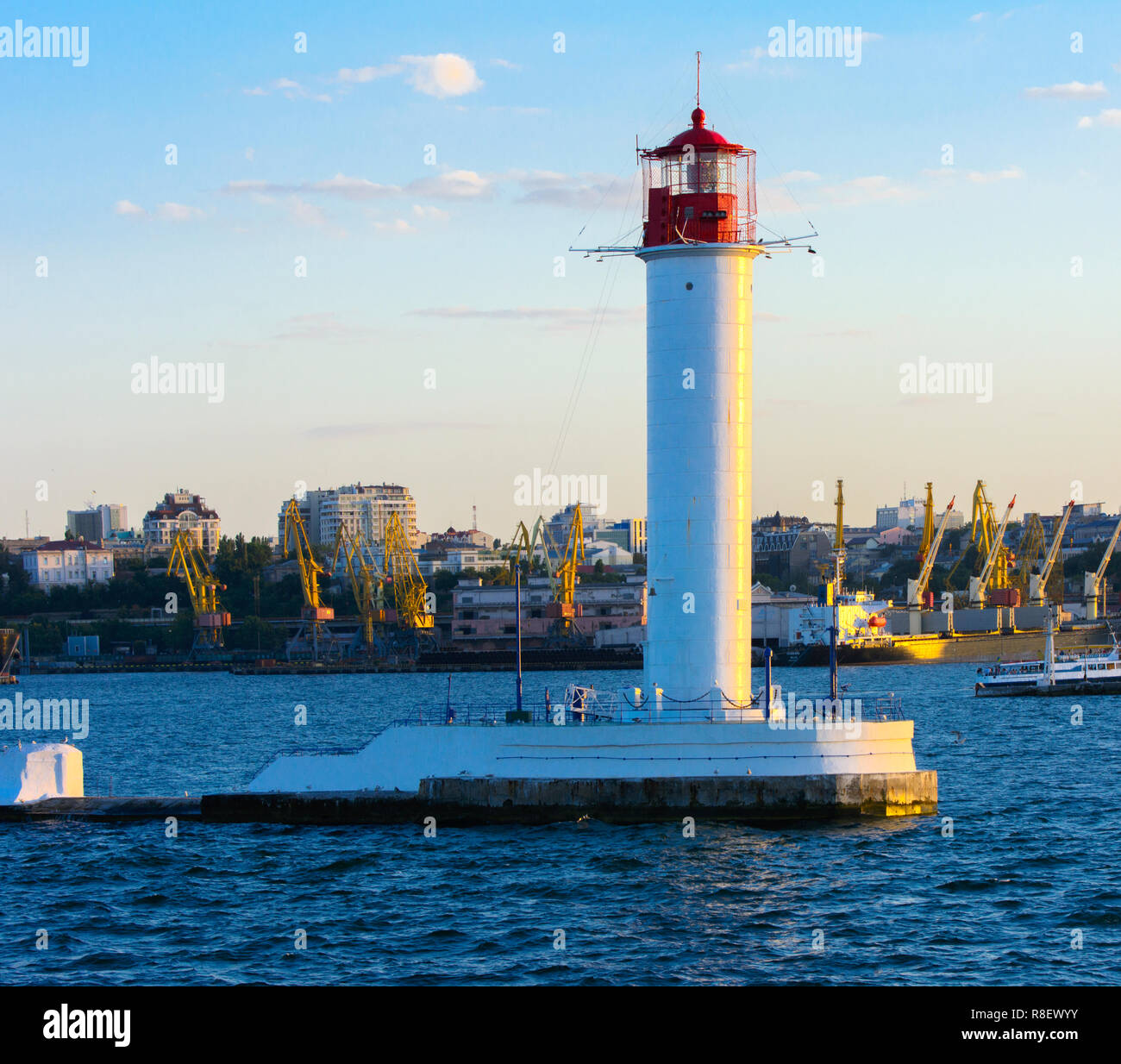 Ein Leuchtturm im Meer am Eingang zum Hafen vor dem Hintergrund eines schönen Abends blauer Himmel in weichen Farben. Sommer Seascape. Weiße Leucht Stockfoto
