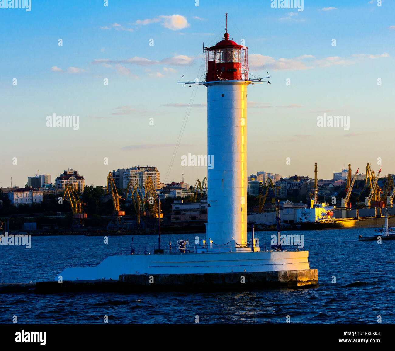 Ein Leuchtturm im Meer am Eingang zum Hafen vor dem Hintergrund eines schönen Abends blauer Himmel in weichen Farben. Sommer Seascape. Weiße Leucht Stockfoto