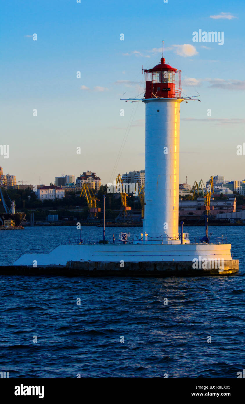 Ein Leuchtturm im Meer am Eingang zum Hafen vor dem Hintergrund eines schönen Abends blauer Himmel in weichen Farben. Sommer Seascape. Weiße Leucht Stockfoto