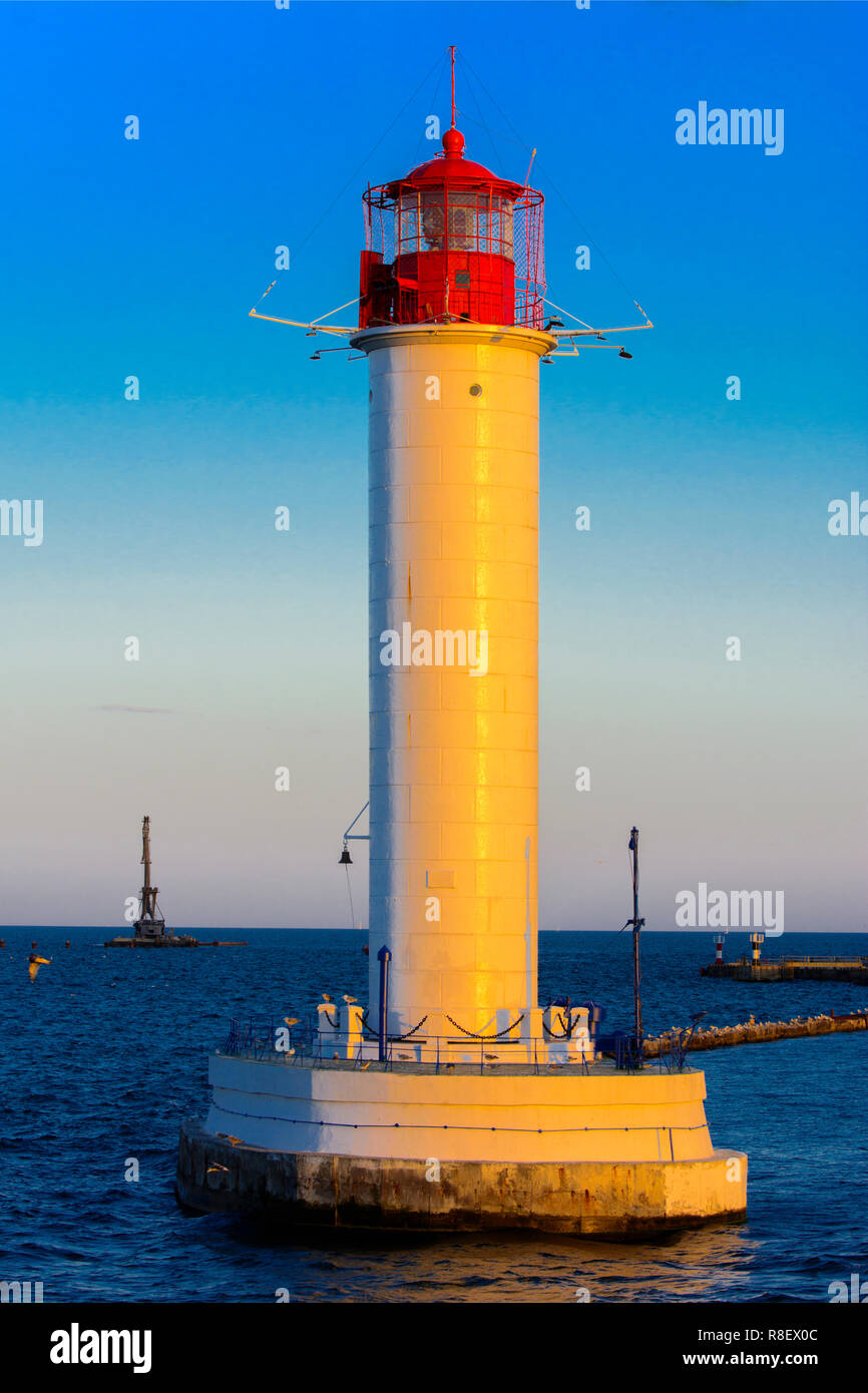 Ein Leuchtturm im Meer am Eingang zum Hafen vor dem Hintergrund eines schönen Abends blauer Himmel in weichen Farben. Sommer Seascape. Weiße Leucht Stockfoto