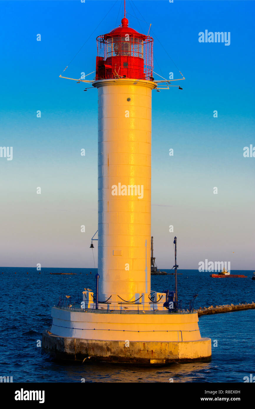 Ein Leuchtturm im Meer am Eingang zum Hafen vor dem Hintergrund eines schönen Abends blauer Himmel in weichen Farben. Sommer Seascape. Weiße Leucht Stockfoto