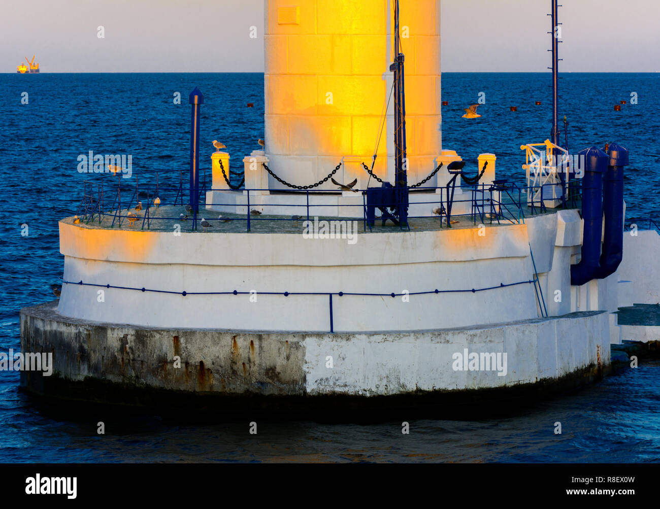 Der untere Teil der Leuchtturm an der Einfahrt zum Hafen auf dem Hintergrund eines schönen Abends blauer Himmel in weichen Farben. Sommer Seascape. Weiße Leucht Stockfoto