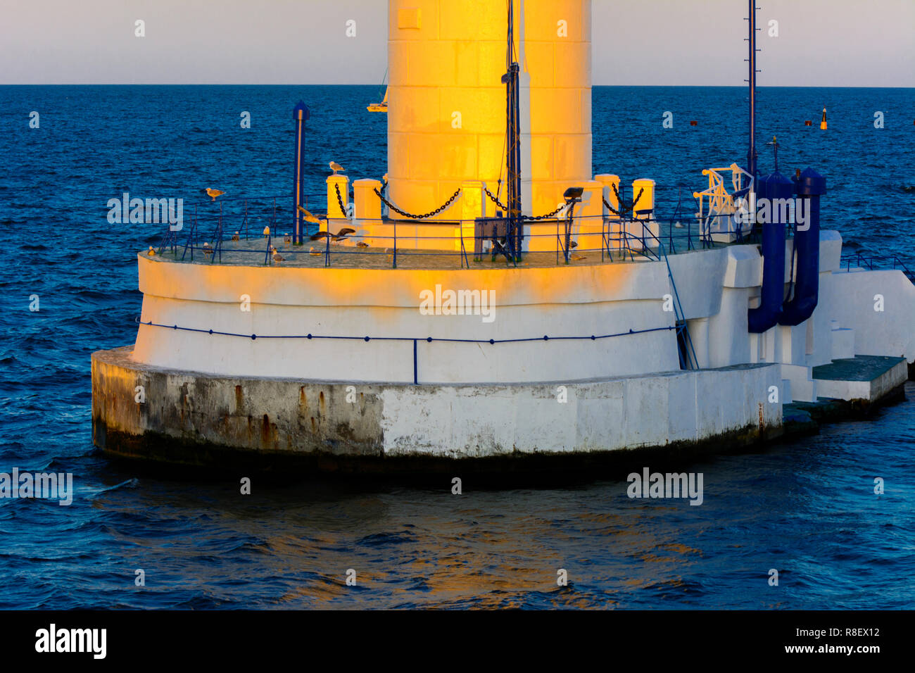 Der untere Teil der Leuchtturm an der Einfahrt zum Hafen auf dem Hintergrund eines schönen Abends blauer Himmel in weichen Farben. Sommer Seascape. Weiße Leucht Stockfoto