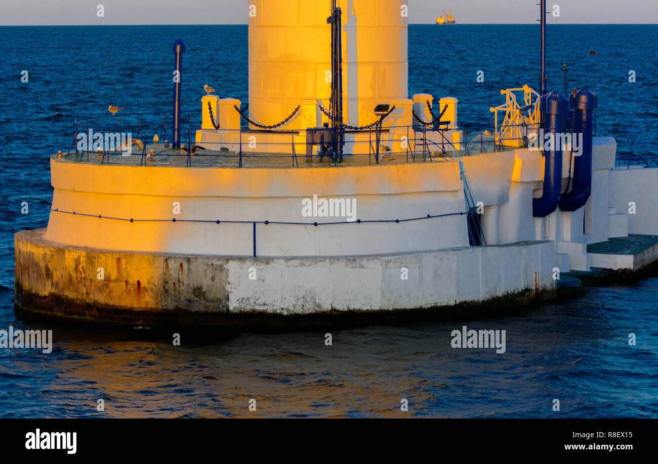Der untere Teil der Leuchtturm an der Einfahrt zum Hafen auf dem Hintergrund eines schönen Abends blauer Himmel in weichen Farben. Sommer Seascape. Weiße Leucht Stockfoto