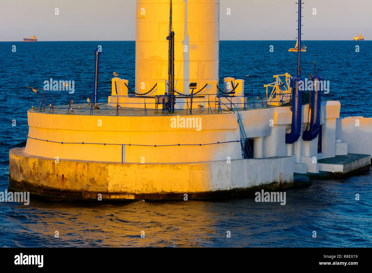 Der untere Teil der Leuchtturm an der Einfahrt zum Hafen auf dem Hintergrund eines schönen Abends blauer Himmel in weichen Farben. Sommer Seascape. Weiße Leucht Stockfoto