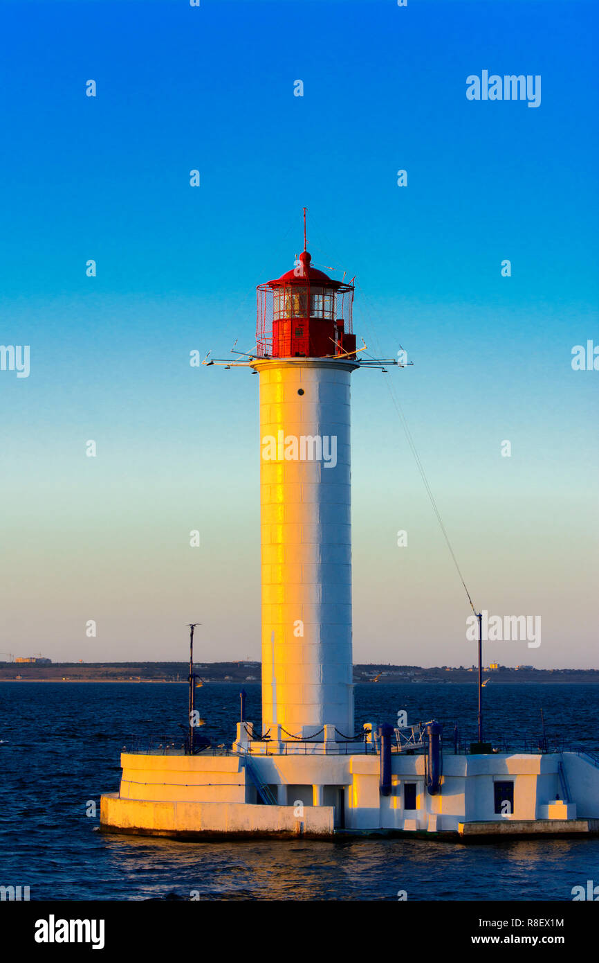 Ein Leuchtturm im Meer am Eingang zum Hafen vor dem Hintergrund eines schönen Abends blauer Himmel in weichen Farben. Sommer Seascape. Weiße Leucht Stockfoto