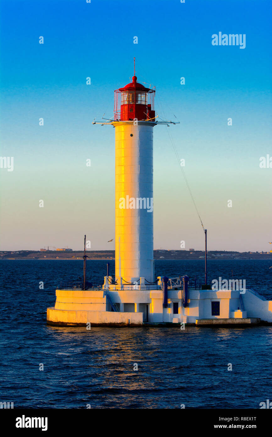 Ein Leuchtturm im Meer am Eingang zum Hafen vor dem Hintergrund eines schönen Abends blauer Himmel in weichen Farben. Sommer Seascape. Weiße Leucht Stockfoto