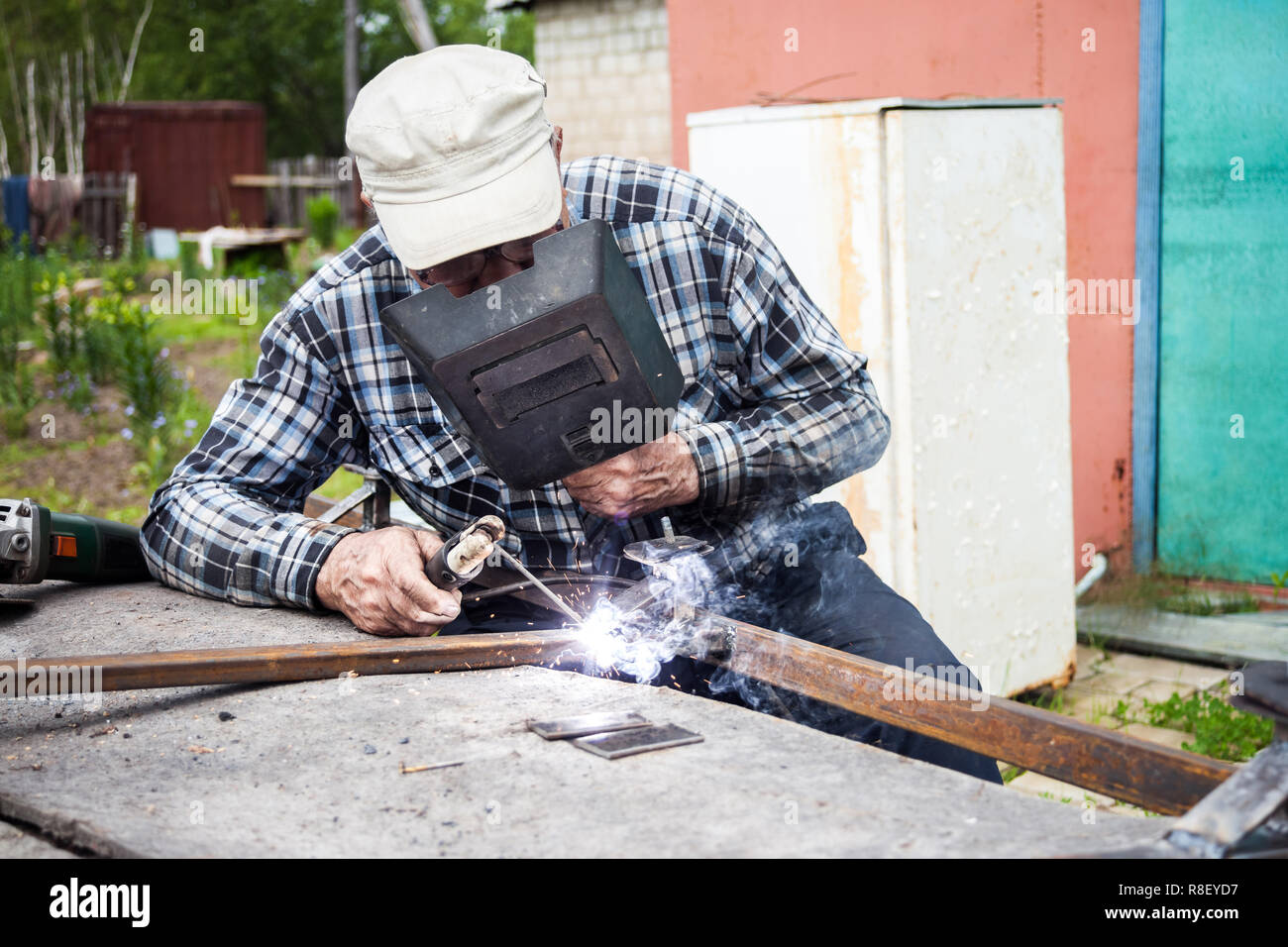 Alter Mann Schweißarbeiten Metallkonstruktion in seinem Garten Stockfoto