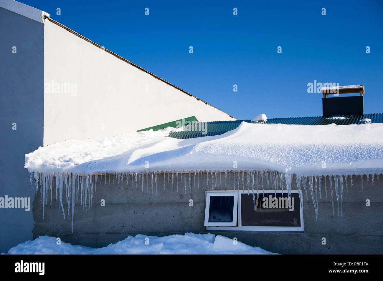 Myvatn, Island. Gebäude fast durch tiefe Schneeverwehungen abgedeckt. Eiszapfen hängen von der Dachterrasse, strahlend blauen Himmel Hintergrund Stockfoto