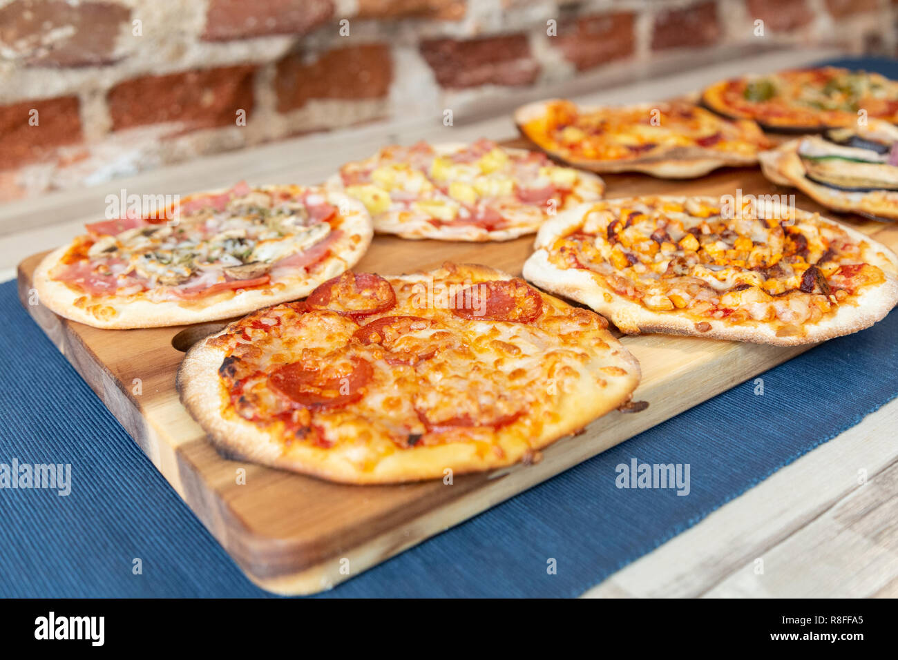 Sieben kleine Pizzen auf einem Holzbrett, frisch aus dem Ofen, bereit, im Restaurant zu essen. Der Fokus liegt auf Pepperoni Pizza. Auf einer hölzernen Tisch mit einem b Stockfoto