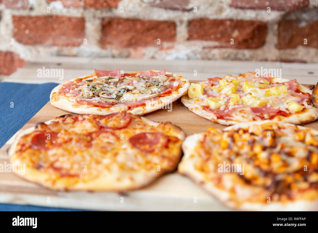 Vier kleine Pizzen auf einem Holzbrett, frisch aus dem Ofen, bereit, im Restaurant zu essen. Fokus auf carbonara Pizza. Auf einem Holztisch mit einem blauen Tabl Stockfoto