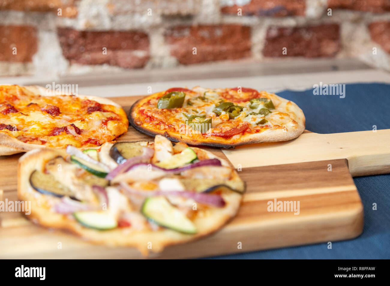 Sieben kleine Pizzen auf einem Holzbrett, frisch aus dem Ofen, bereit, im Restaurant zu essen. Mit dem Fokus auf chili Pizza. Auf einem Holztisch mit einem blauen t Stockfoto