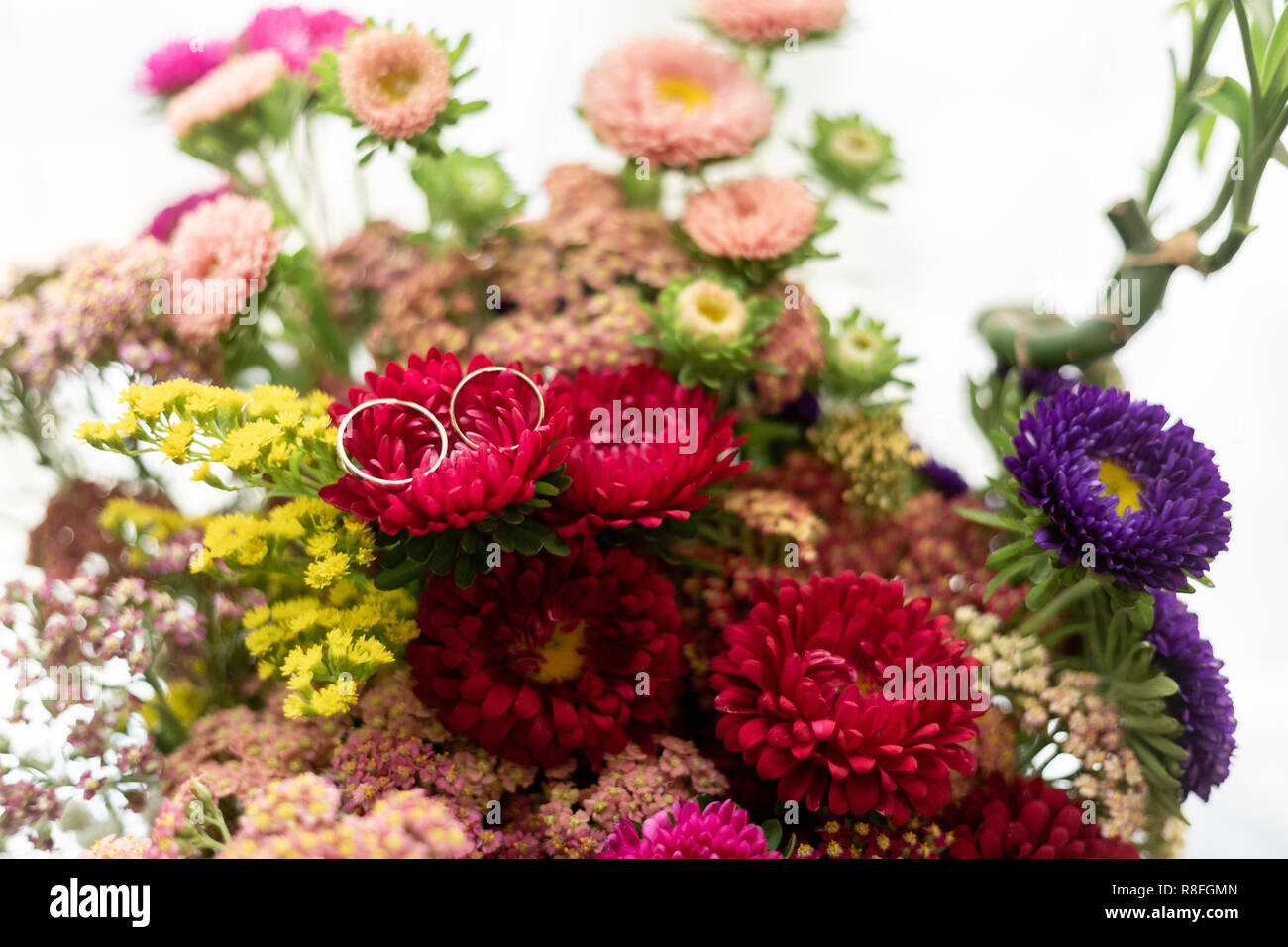 Zwei goldene Ringe von Braut und Bräutigam auf eine Blume von einem bunten Blumenstrauß Stockfoto