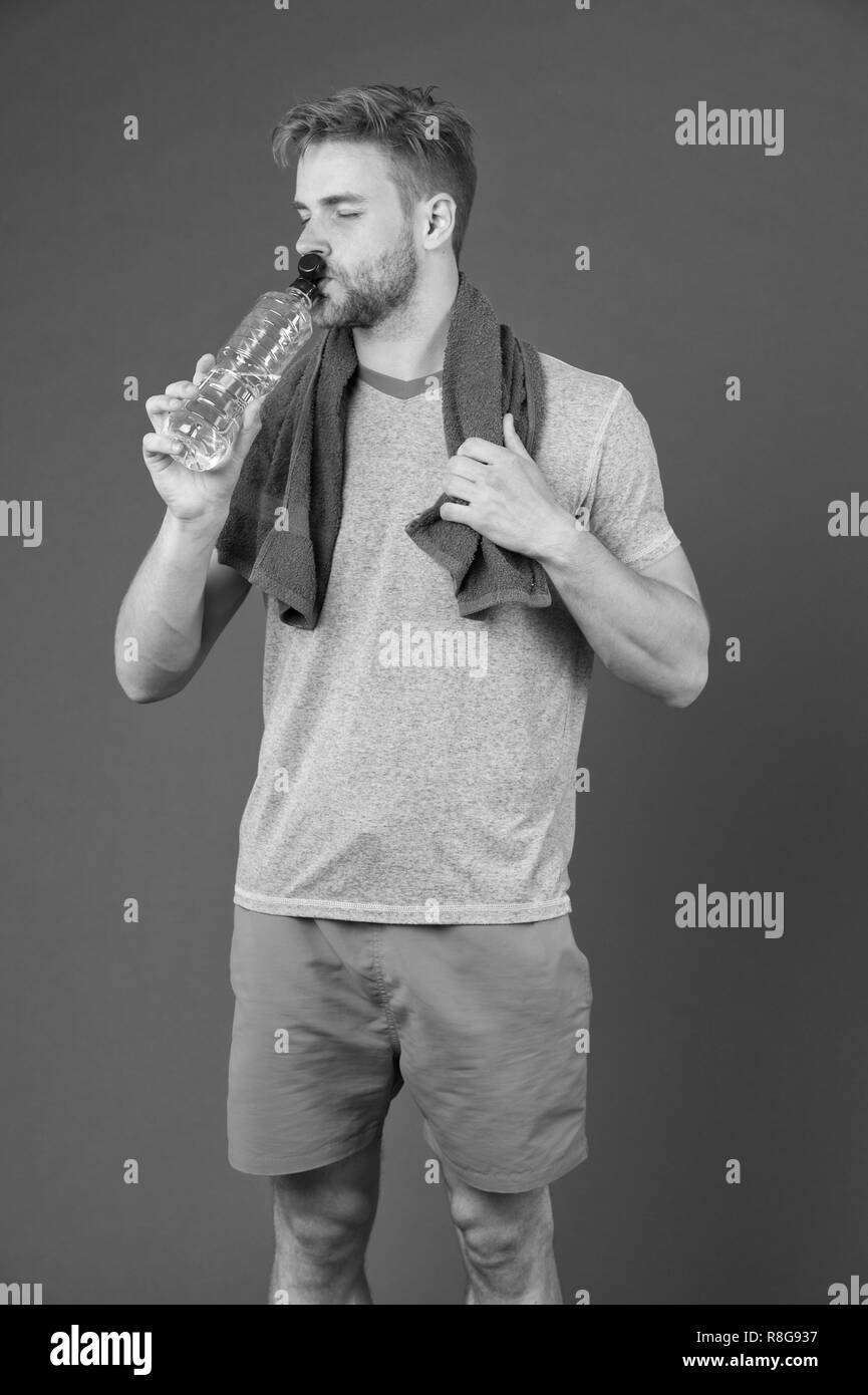 Man Wasser trinken nach dem Training auf Violett Hintergrund. Durstige Sportler mit Kunststoff Flasche auf lila Hintergrund. Durst und Austrocknung. Trinkwasser für die Gesundheit. Sportliche Aktivität und Energie. Stockfoto