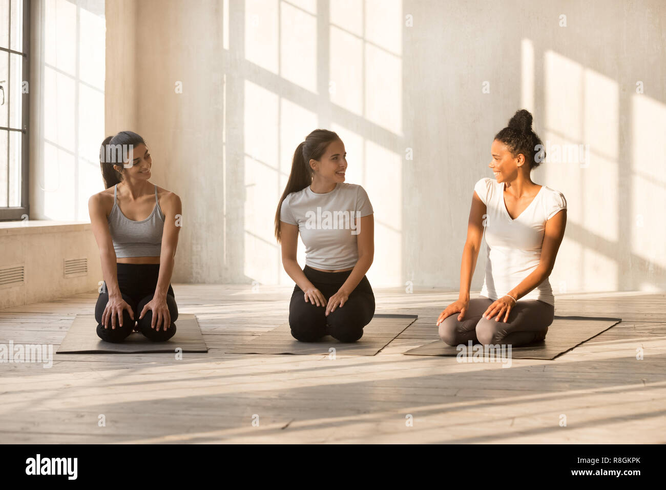 Hübsche Frauen sprechen, sitzen auf Yoga Matte vor dem Trainin Stockfoto
